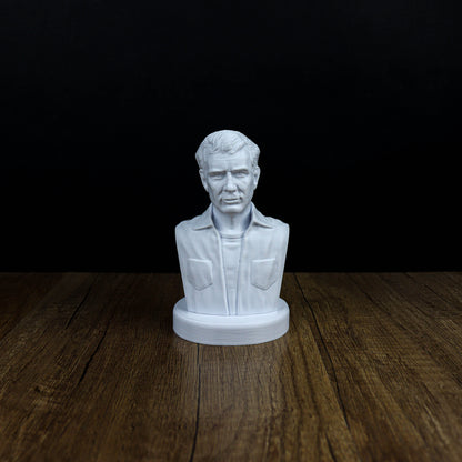 A white bust of a man is displayed on a wooden surface against a black background.