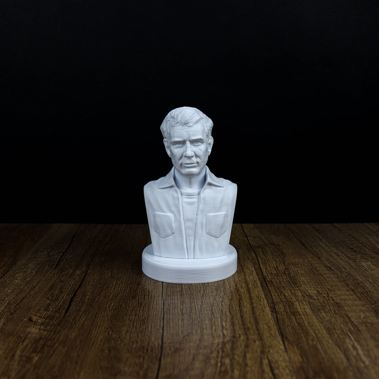 A white bust of a man is displayed on a wooden surface against a black background.