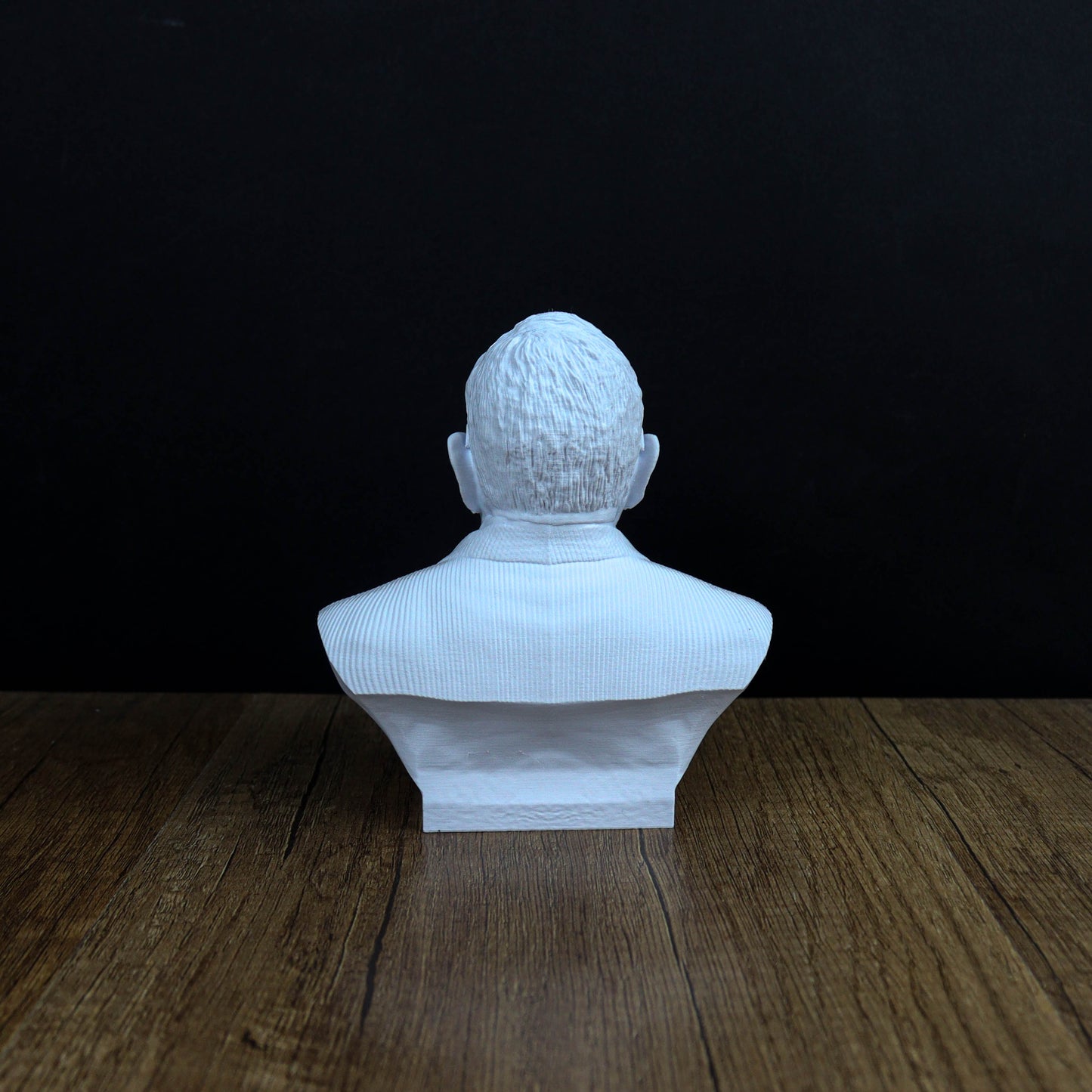 A white bust of a person's head is displayed on a wooden surface against a black background.