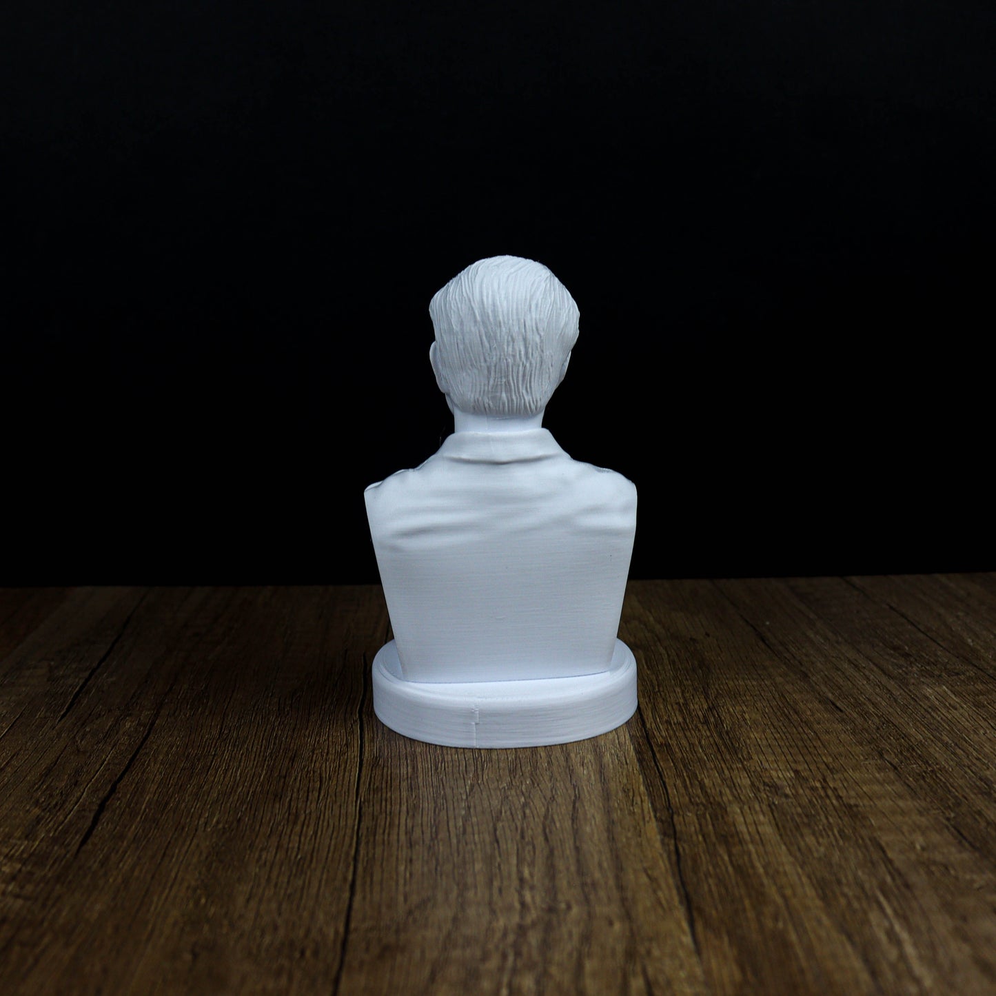 A white bust of a person is sitting on a wooden surface against a black background.