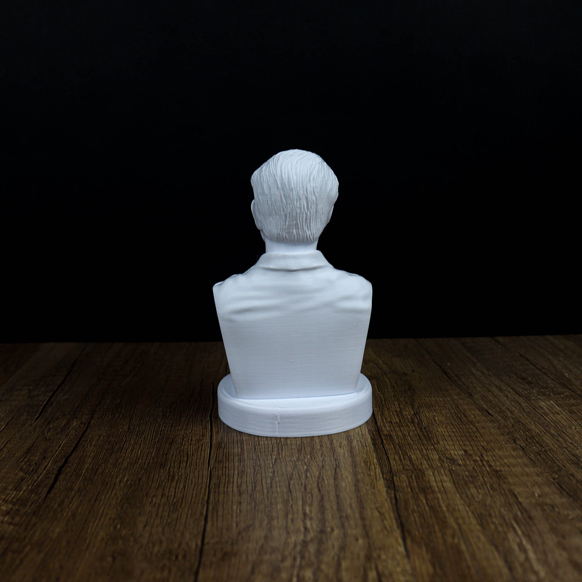 A white bust of a person is sitting on a wooden surface against a black background.