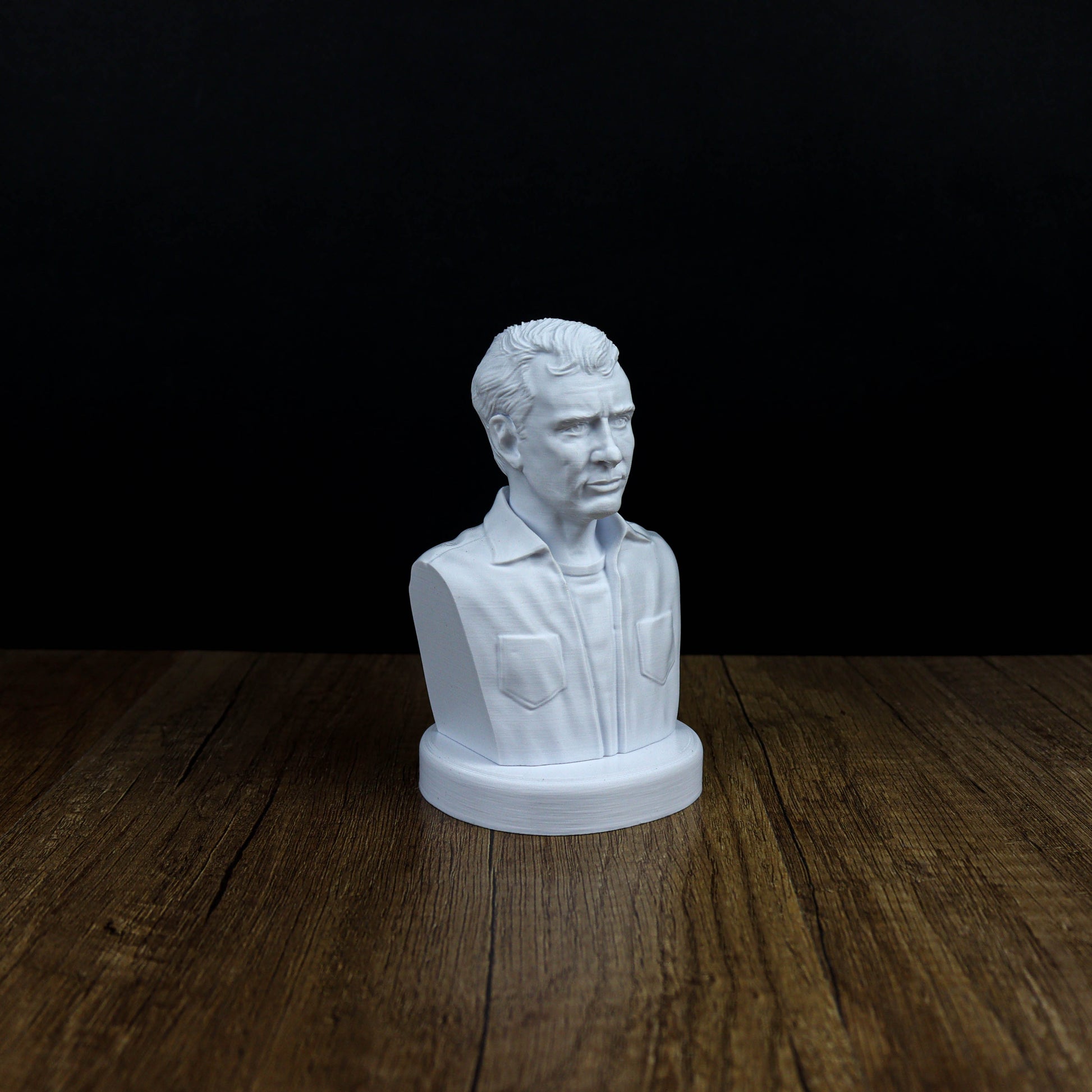 A white bust of a man is displayed on a wooden surface against a black background.