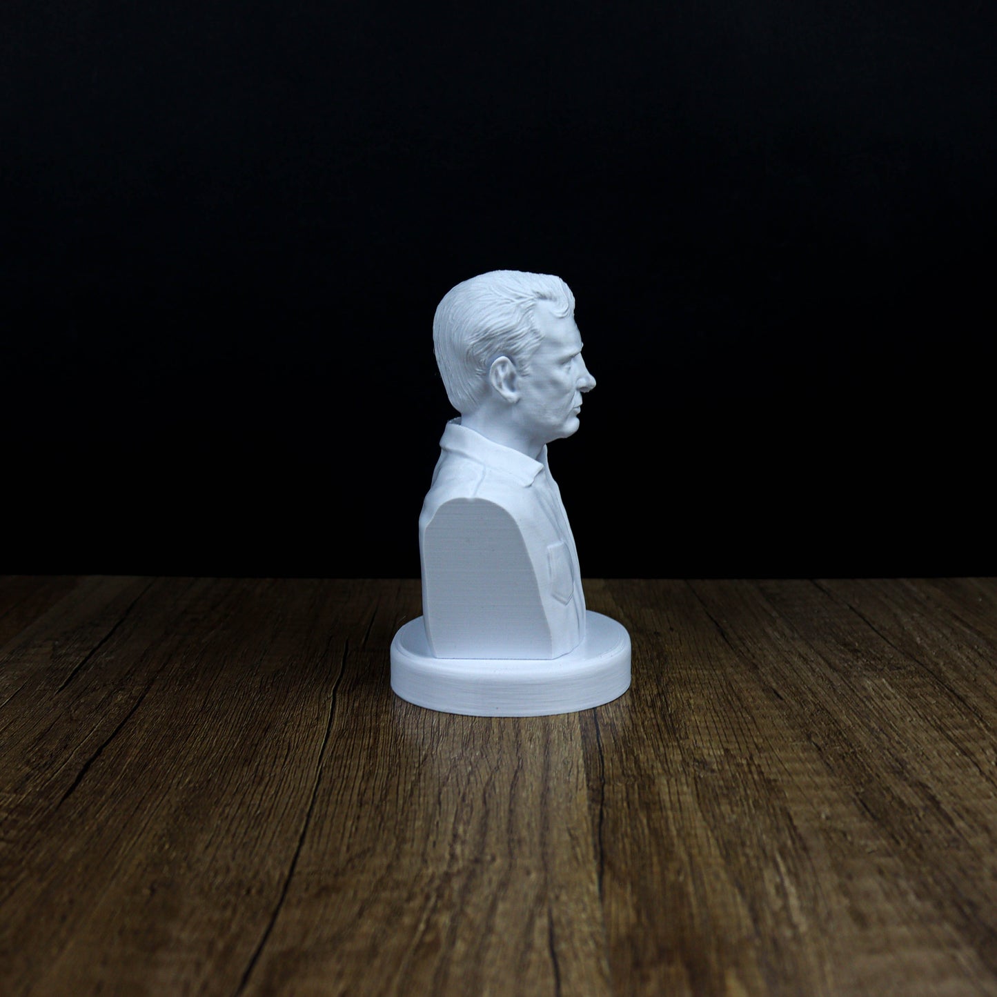 A white bust of a man's head is displayed on a wooden surface against a dark background.