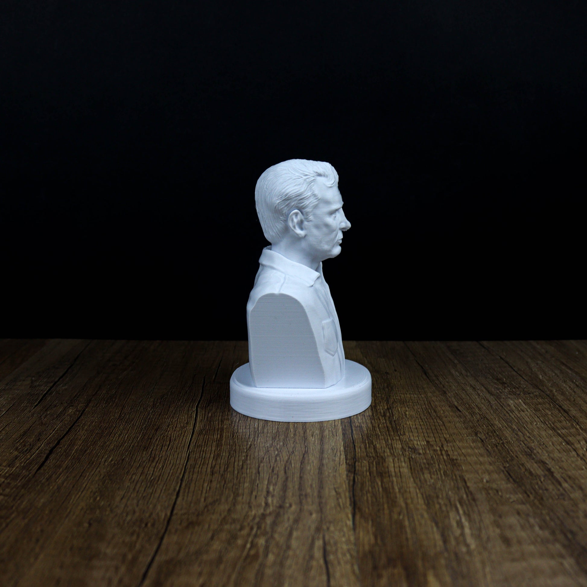 A white bust of a man's head is displayed on a wooden surface against a dark background.